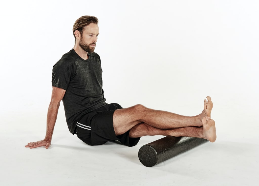 man massages calves with a foam roller to ease tension