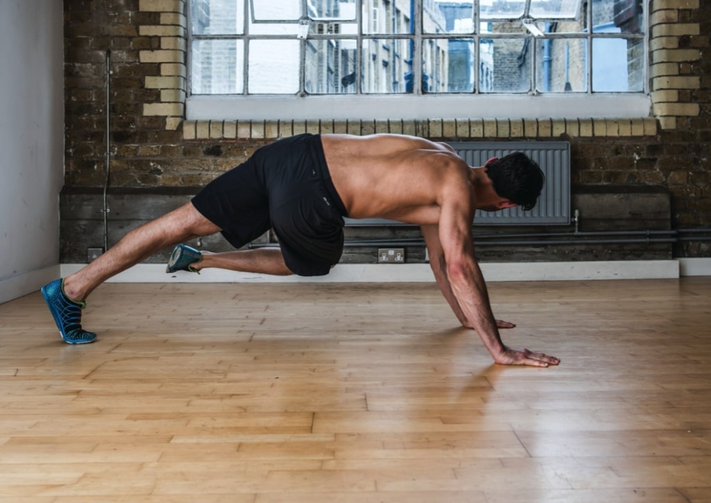 Man performing second part of single-leg knee twist – one of the best plank variations