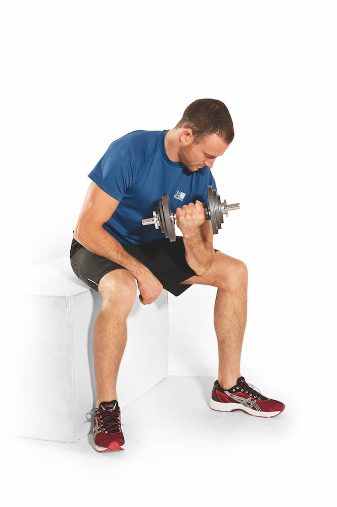man performing dumbbell concentration curl as part of a home dumbbell arms workout