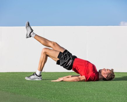 man in red top and black shorts performing single-leg glute bridge as part of a strength workout for runners