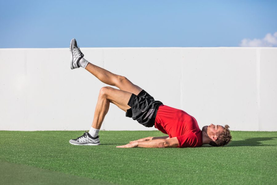 man in red top and black shorts performing single-leg glute bridge as part of a strength workout for runners