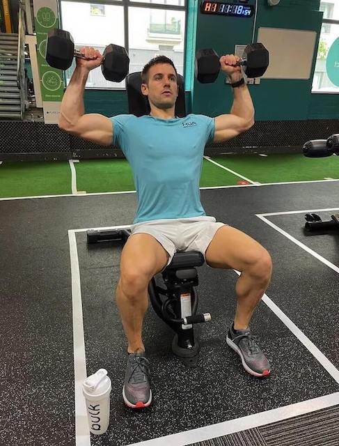 man in turquoise t-shirt performing dumbbell shoulder press as part of a 30-minute upper-body workout