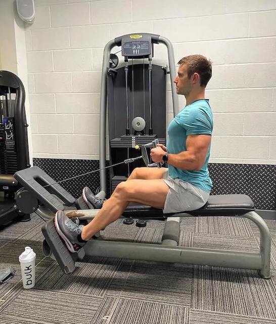 man in turquoise t-shirt and grey shorts performing seated row in gym as part of a 30-minute upper-body workout