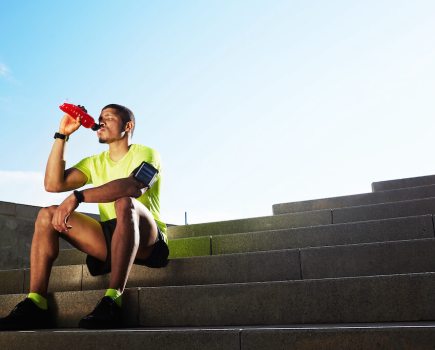 Athletic man sat on outside steps drinking bottle of water
