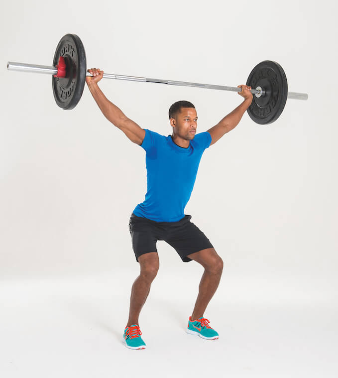 man in blue t-shirt and shorts performing overhead squat with barbell