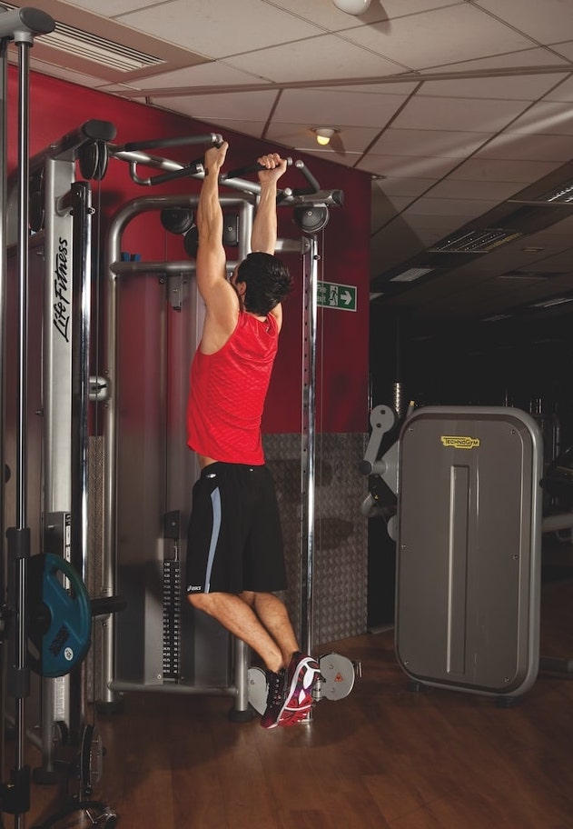 man in red vest and shorts performing the first stage of a chin-up in the gym