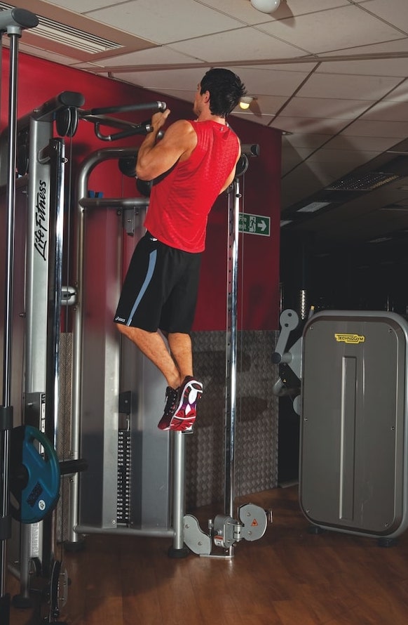 man in red vest and shorts performing the second stage of a chin-up in the gym