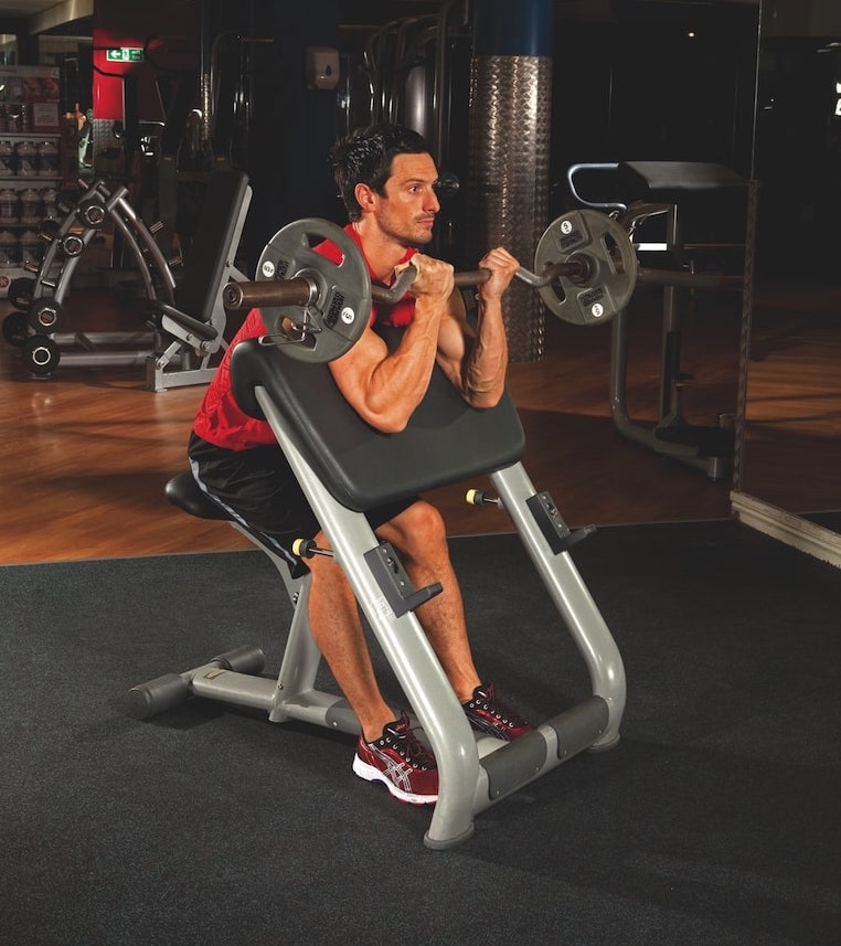 man in red vest and shorts performing the second stage of a EZ bar preacher curl in the gym