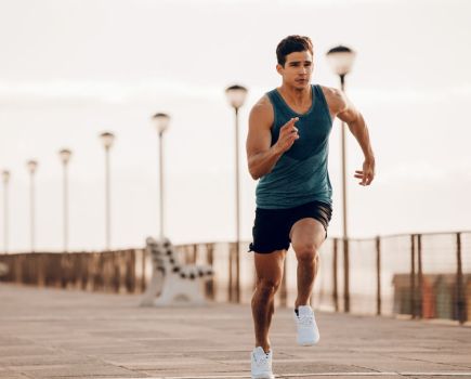 fit man in vest and shorts running quickly along a promenade