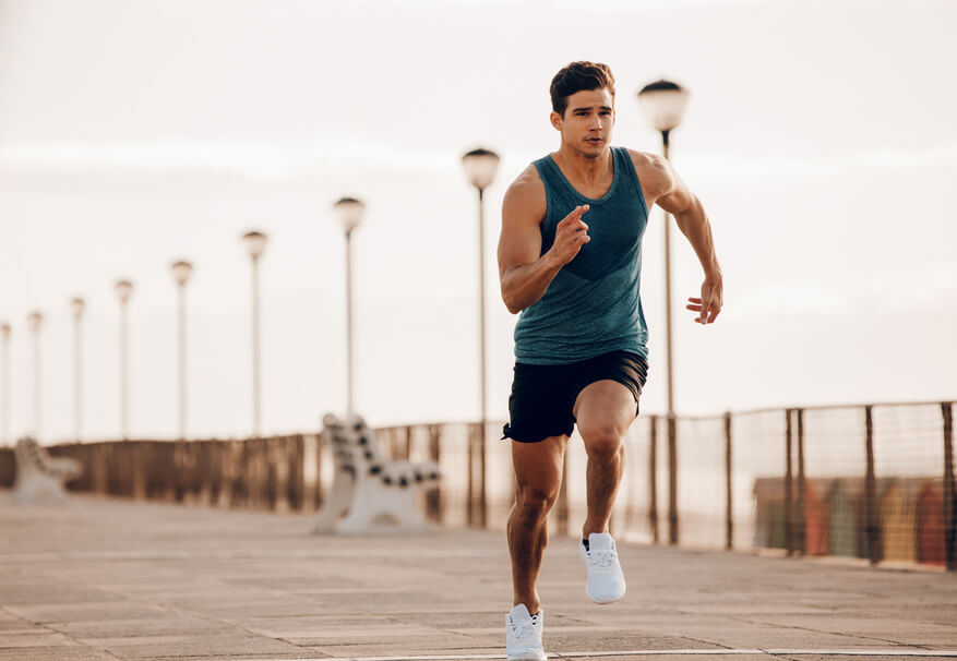 fit man in vest and shorts running quickly along a promenade