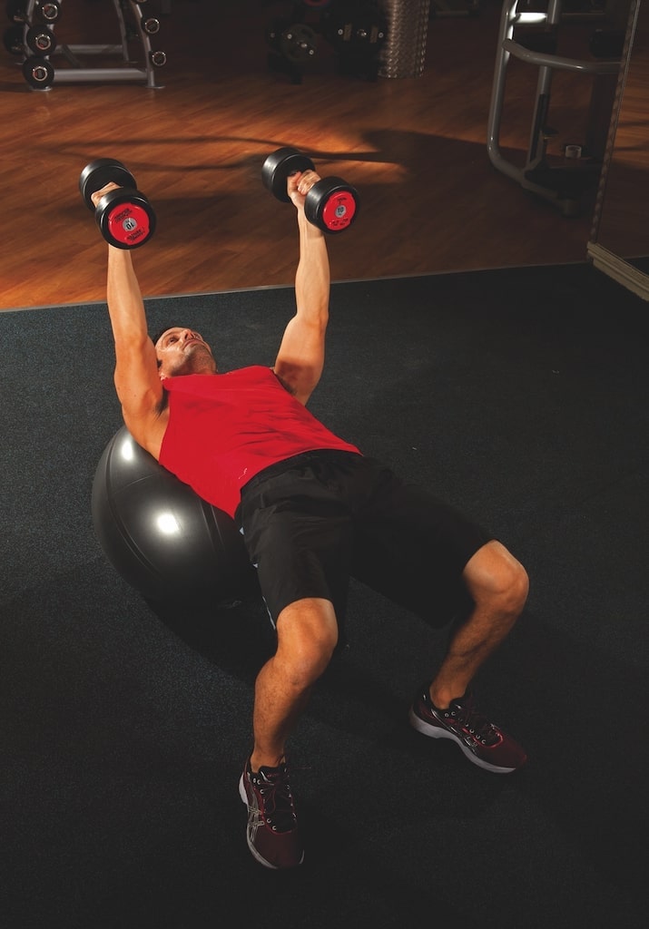 man in red vest and shorts performing the first stage of a Swiss ball dumbbell triceps extension