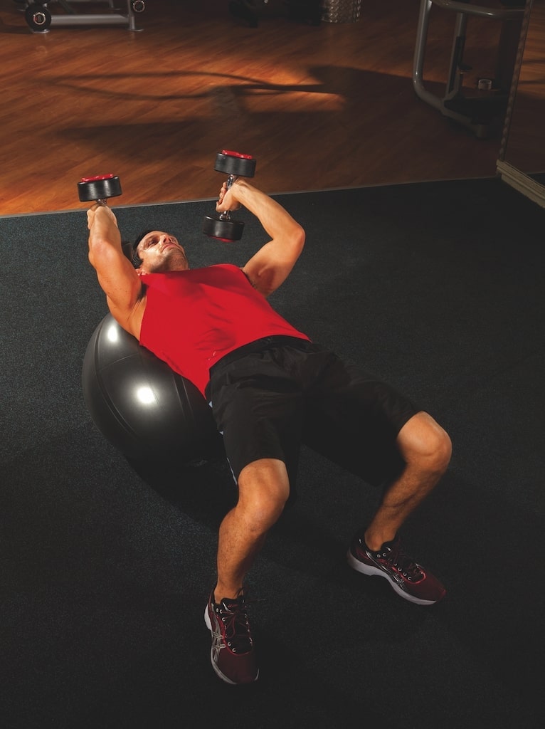 man in red vest and shorts performing the second stage of a Swiss ball dumbbell triceps extension