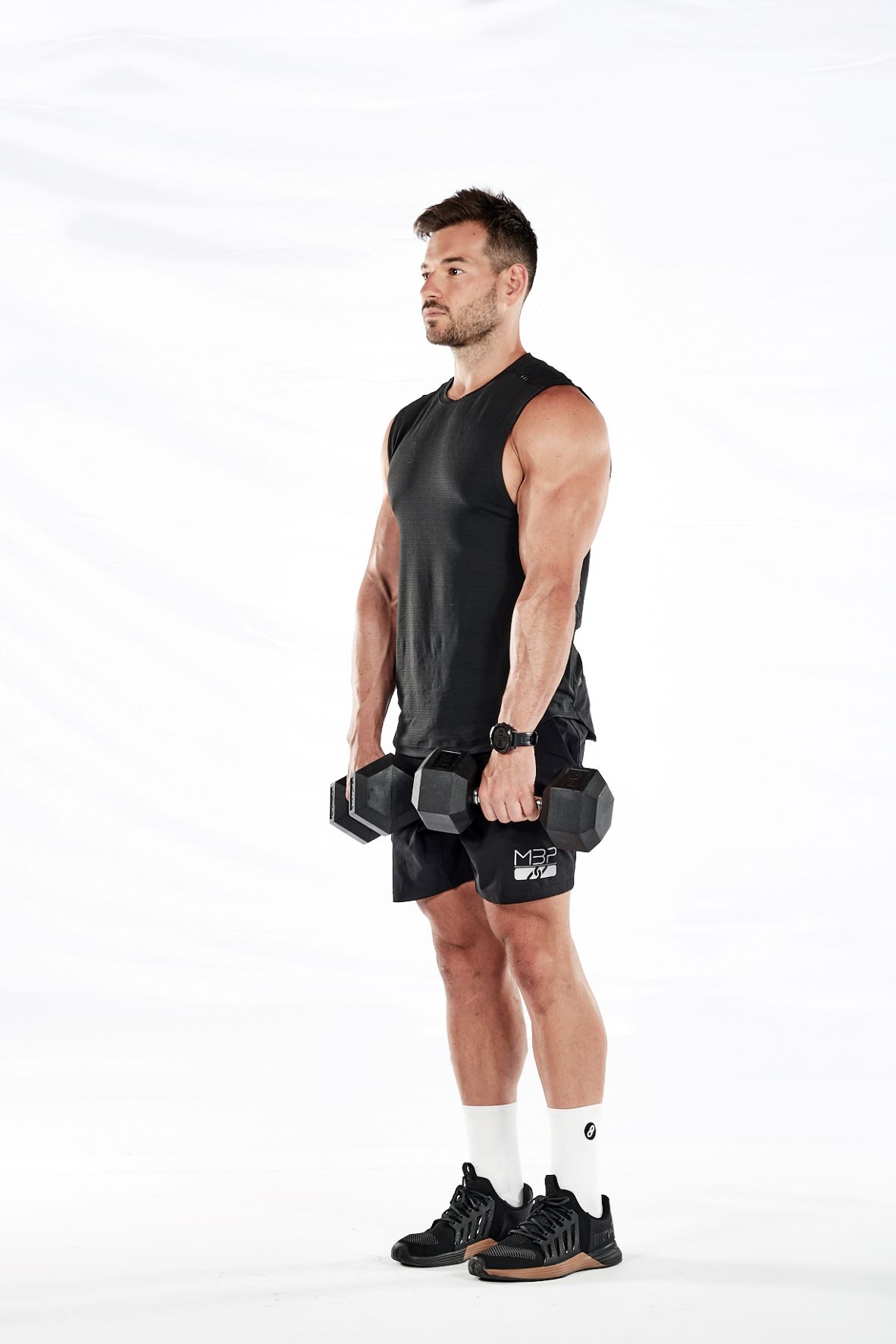 Two stages of the dumbbell deadlift – standing with feet hip-width apart, weights by the hips; leaning and bending the knees to lower dumbbells close to the floor.
