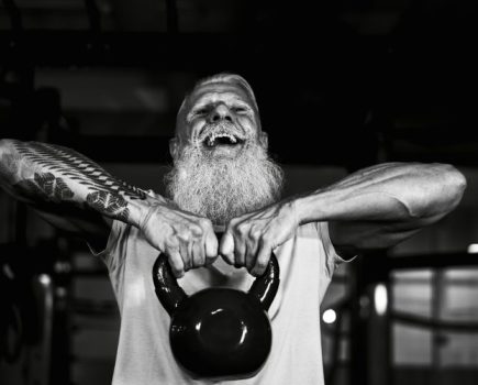 An old man with white hair and beard lifting a kettlebell