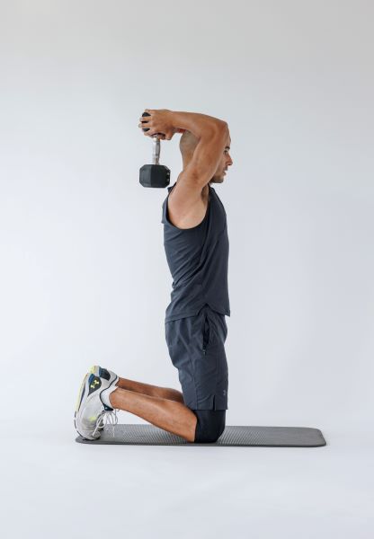 man demonstrating tricep overhead extension: kneeling, he holds a dumbbell behind his head in both hands