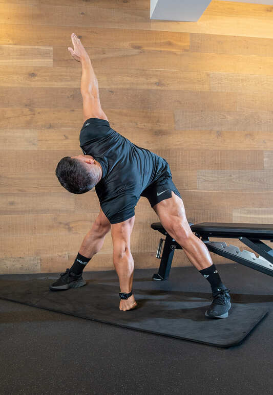 Part of the best full-body dumbbell workout: a man demonstrates t-spine rotations, twisting to the right with arms outstretched