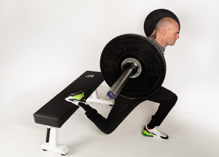 Man lifting barbell with one foot raised on a bench behind - improve your cycling fitness
