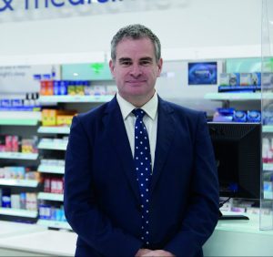A man in a suit and tie standing in front of a pharmacy counter