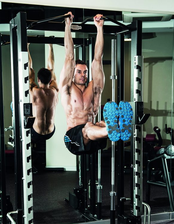 Man in a gym performing the end of a hanging leg raise