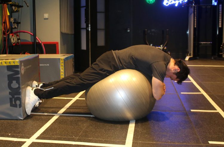 A man performs a gym ball low back hyperextension - best lower back exercises