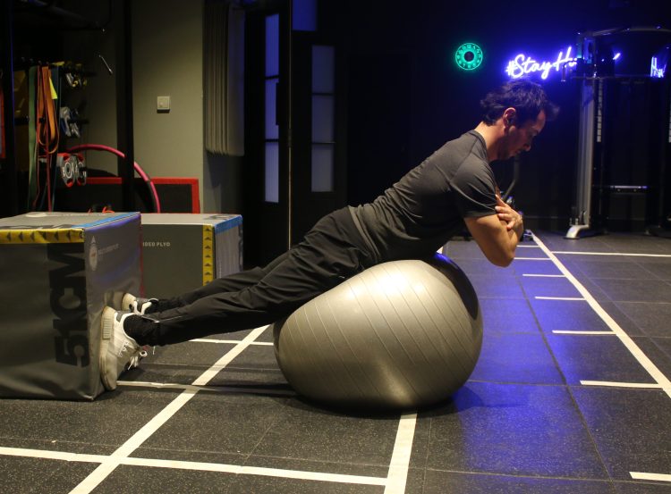 Man performing end of a gym ball low back hyperextension - best lower back exercises