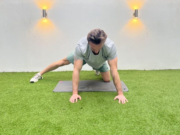man on exercise mat in garden demonstrating adductor rockback, one of the best stretching exercises for beginners