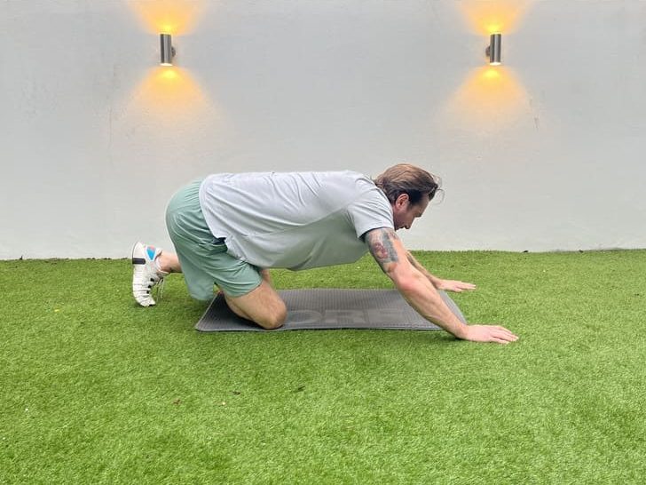 man on exercise mat in garden, demonstrating how to do all fours glute mobilisation stretch for beginners