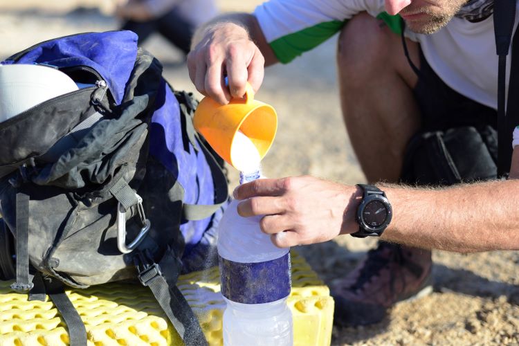 A man pouring electrolyte power into a water bottle outside
