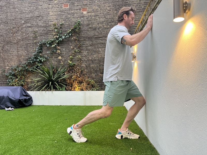 man uses wall in garden to stretch ankle in knee to wall stretching exercises for beginners
