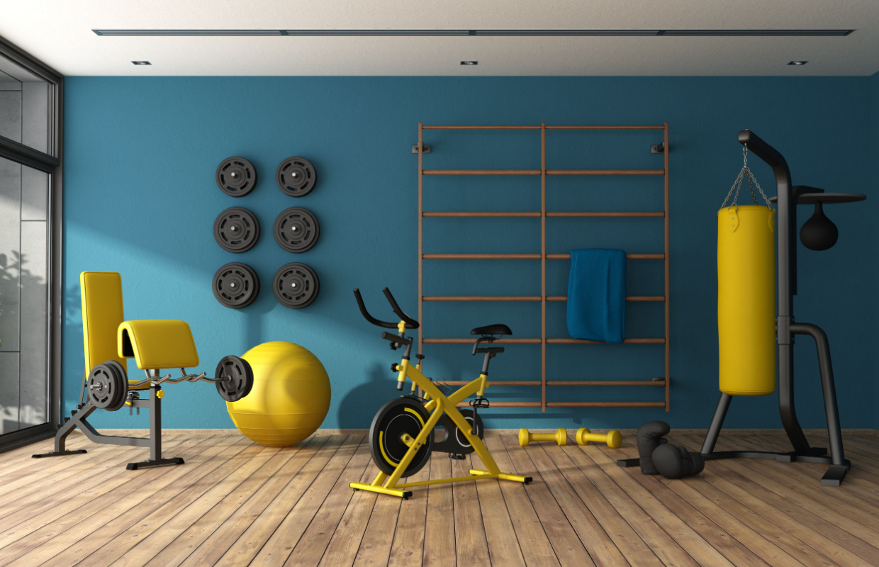home gym set up for workouts. blue wallpaper, wooden floor with yellow gym equipment including punching bag and bench
