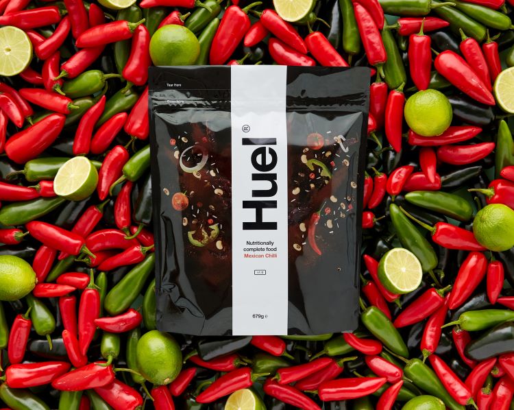 Product shot of a bag of Huel food on a bed of peppers and limes
