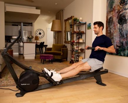 A man in an apartment using the Hydrow Wave rowing machine