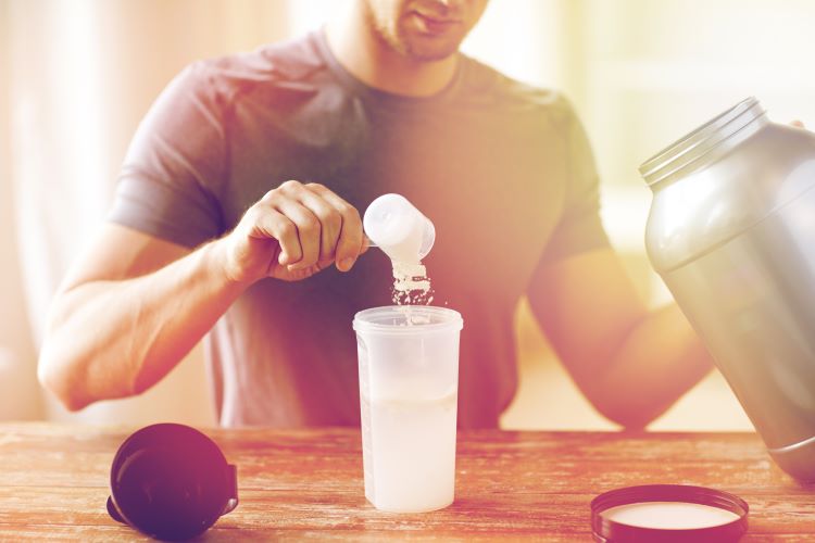 Man at a table measuring out a serving of whey protein powder