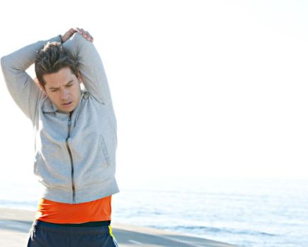 A man in a tracksuit on a beach stretching and warming up