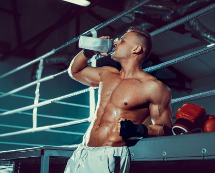 A man outside a boxing ring drinking a clear protein drink