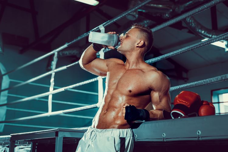 A man outside a boxing ring drinking a clear protein drink