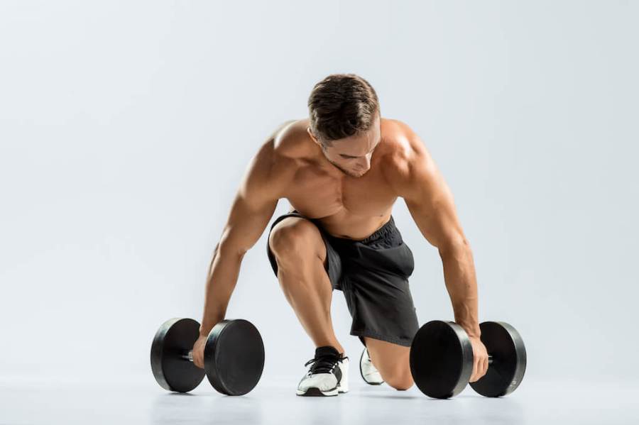 Topless man kneeling on the floor with a pair of dumbbells