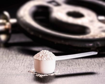 Scoop of creatine powder with weights in the background