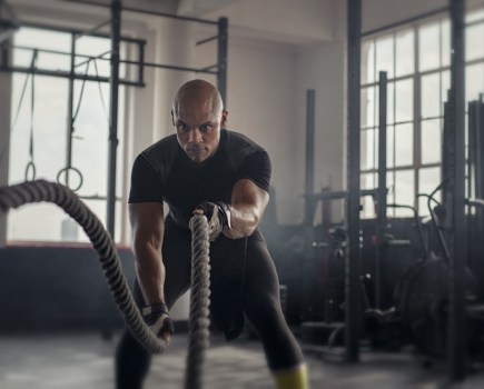 man in gym working out using ropes, wearing black gym shirt