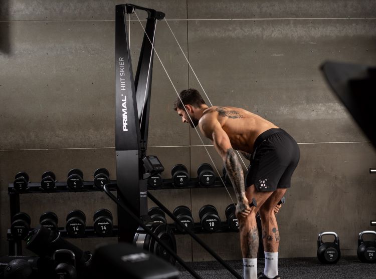 A man in a gym using a Primal Pre Series HIIT Skier cardio machine