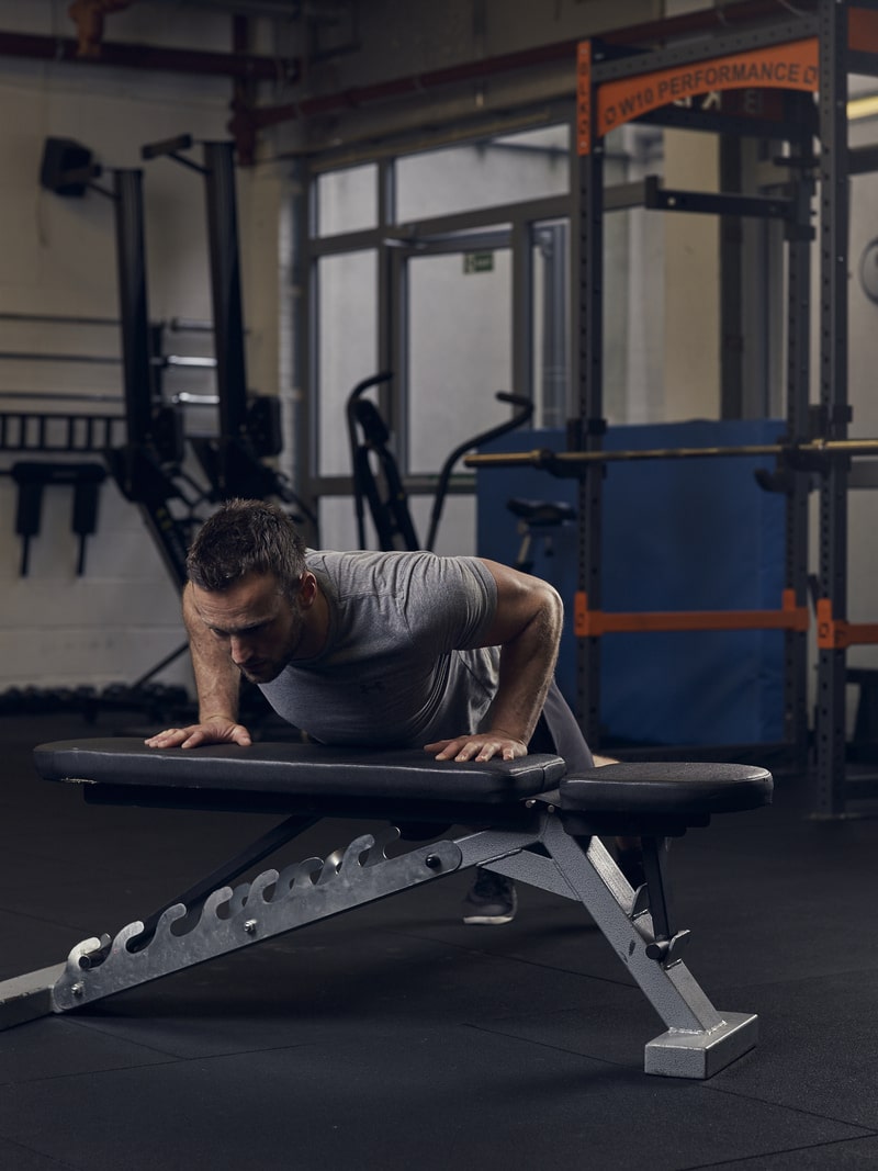 man lowers into incline press up position in the gym using a bench