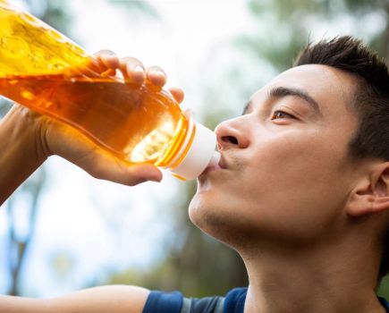 man outside drinking electrolyte drinks from an orange bottle after a run or workout,