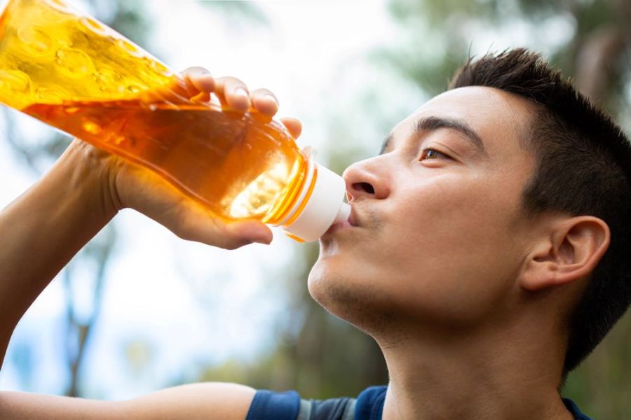 man outside drinking electrolyte drinks from an orange bottle after a run or workout,