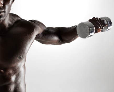 topless man performing dumbbell lateral raise as part of dumbbell shoulder workout