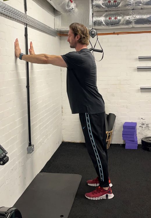 Man performing standing wall press - best back stretches