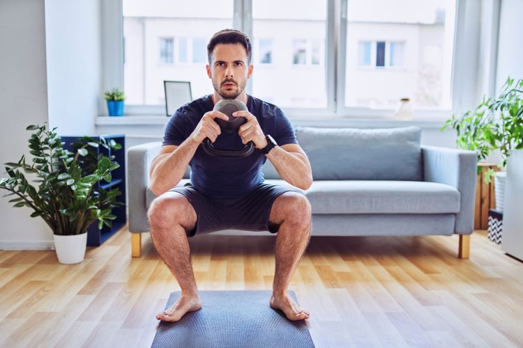 A man at home performing a kettlebell goblet squat