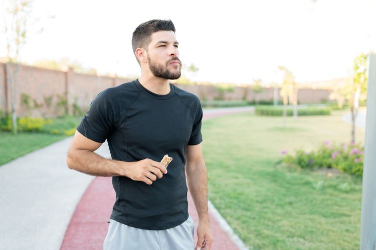 Man by a running track eating a protein bar