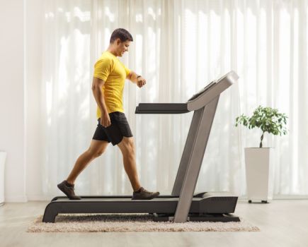 man walking on a treadmill at home, checking his fitness watch