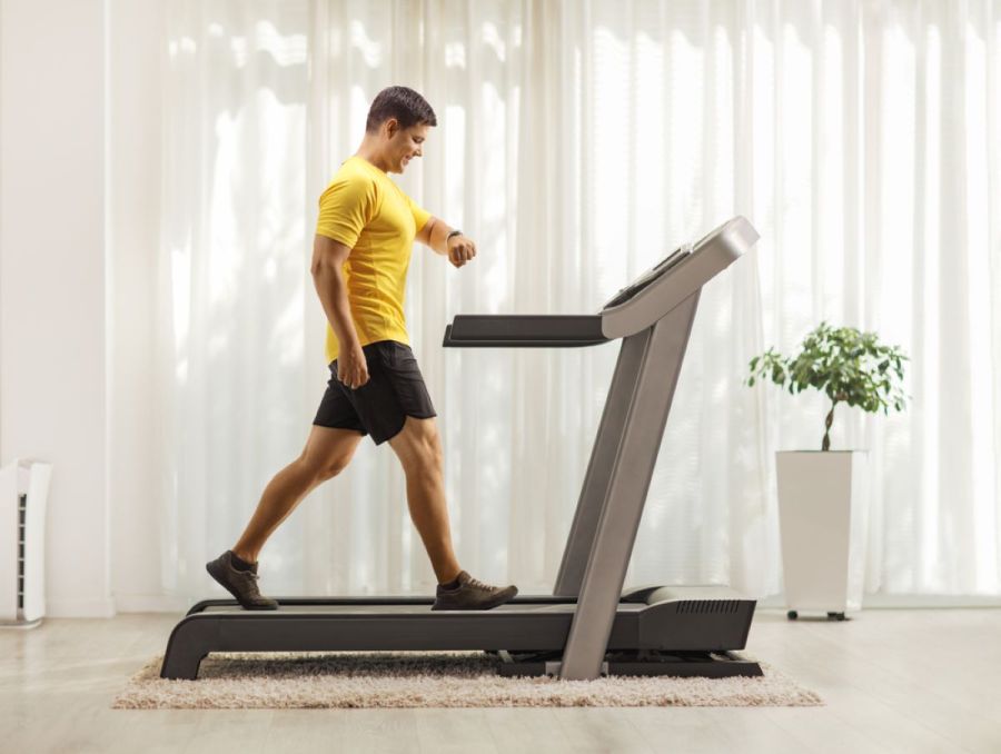 man walking on a treadmill at home, checking his fitness watch