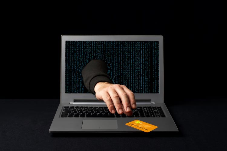 A hand reaching through a laptop screen to steal a credit card